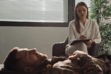 homme allongé lors d'une séance d'hypnose thérapeutique avec une praticienne qui prend des notes